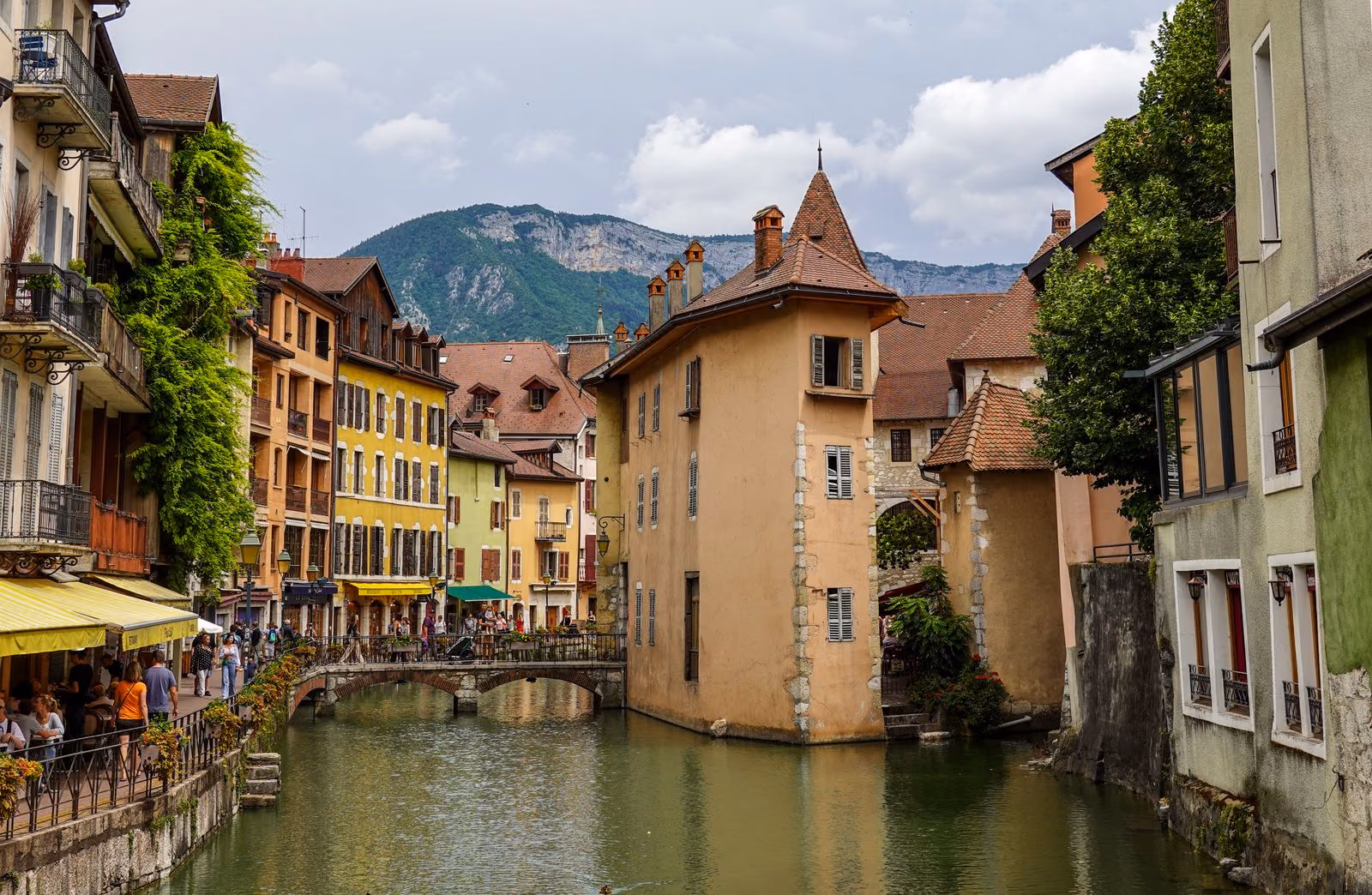 Le Palais de l’Isle au milieu du canal dans la vieille ville d’Annecy, entouré de maisons pastel et de montagnes.