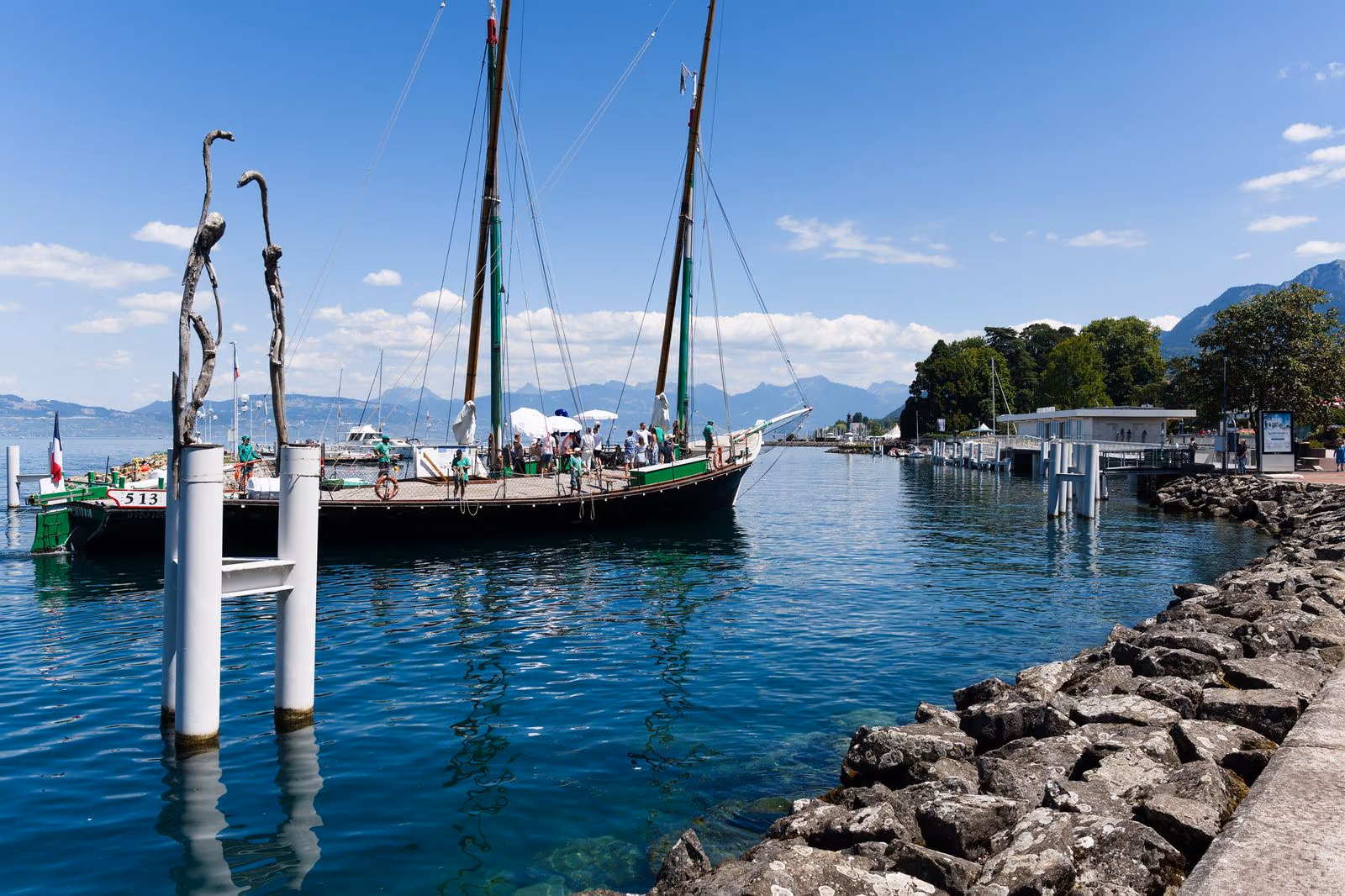 Une barque traditionnelle du Léman amarrée dans le port d’Évian, les Alpes en arrière-plan.