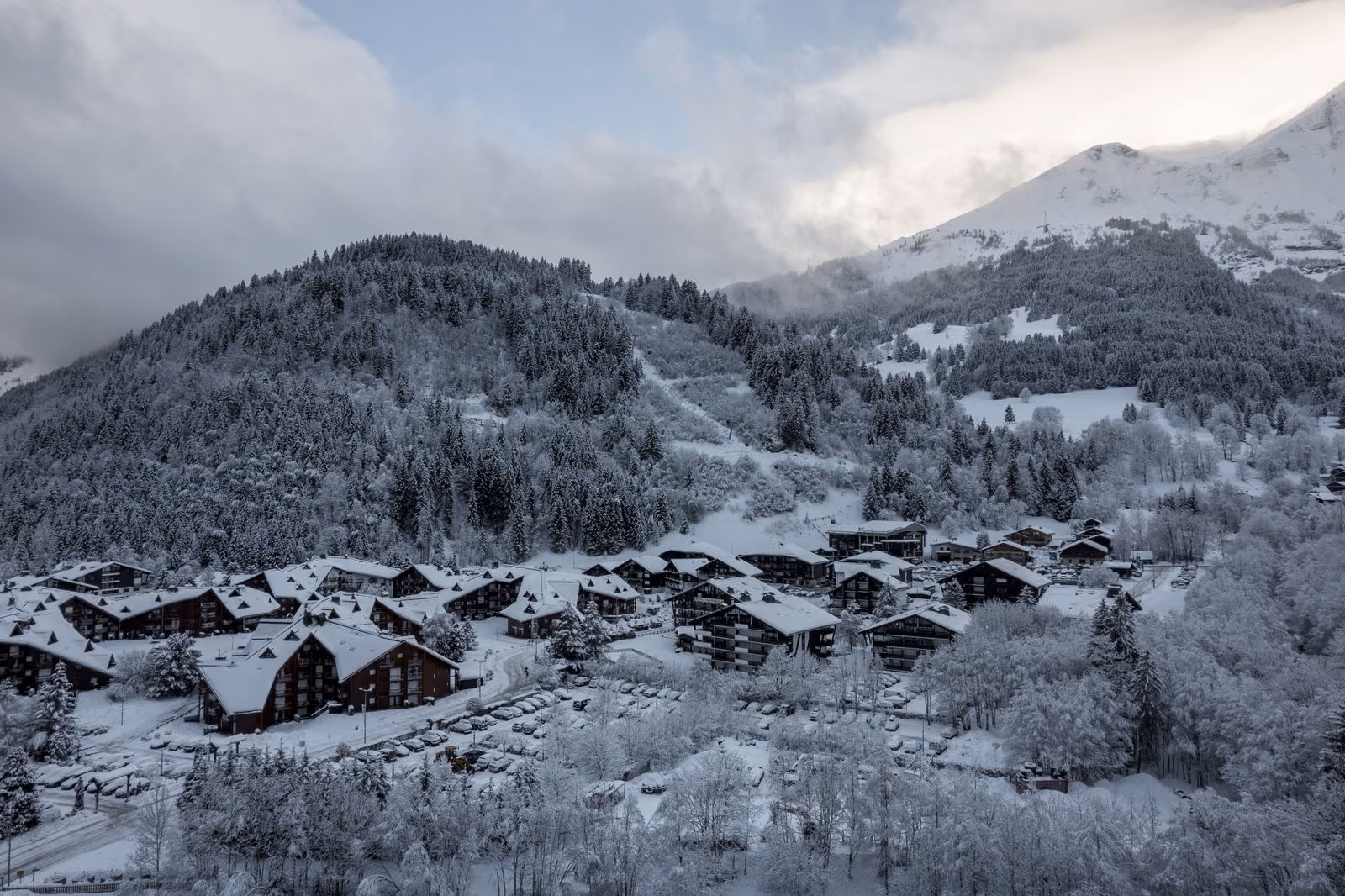 Une station des Alpes françaises sous la neige et les nuages bas, immeubles dispersés parmi les arbres.