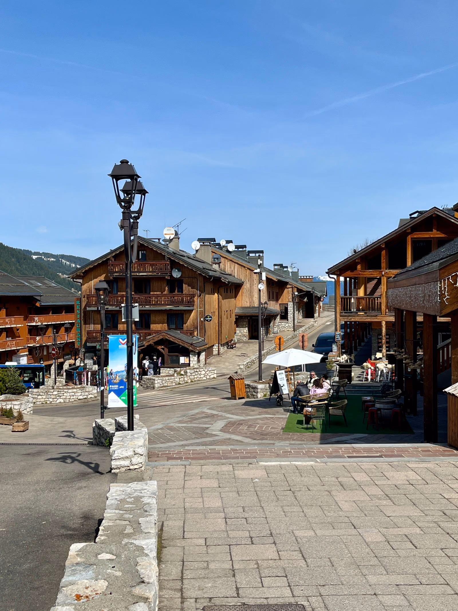 Une rue bordée de chalets et de commerces en bois dans un village de station des Alpes françaises.