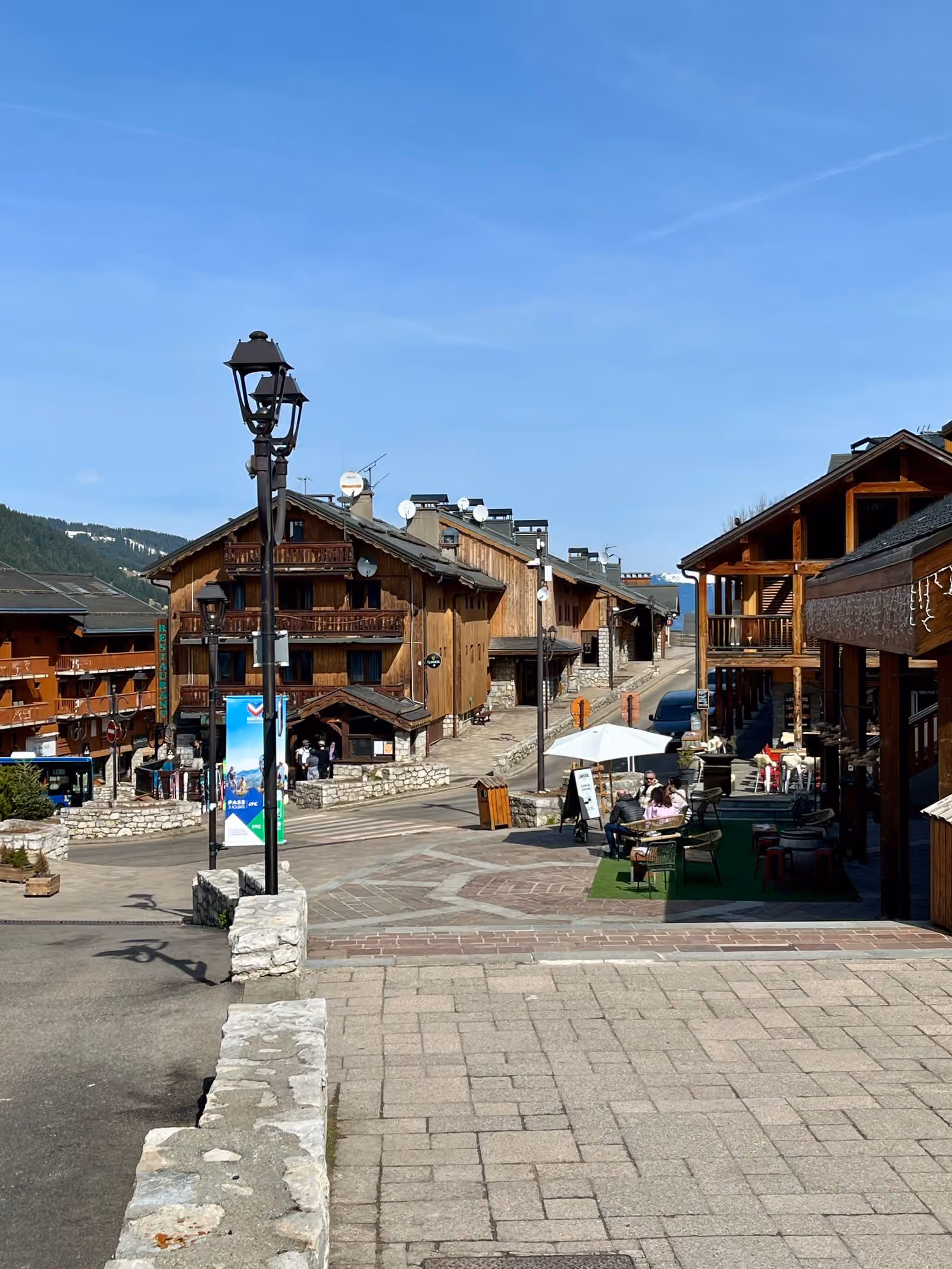 Une rue bordée de chalets et de commerces en bois dans un village de station des Alpes françaises.