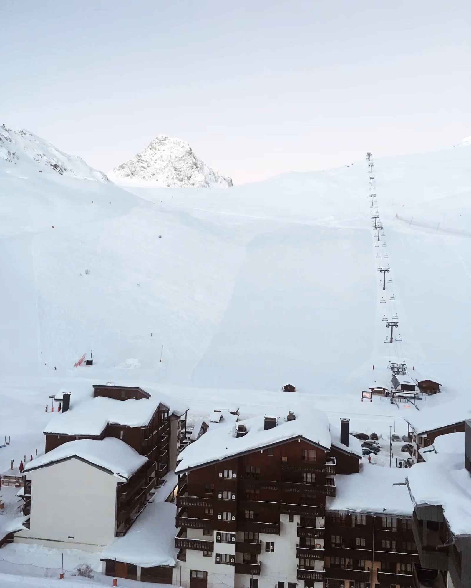 Immeubles enneigés et télésiège s’élevant vers un sommet rocheux à Tignes.