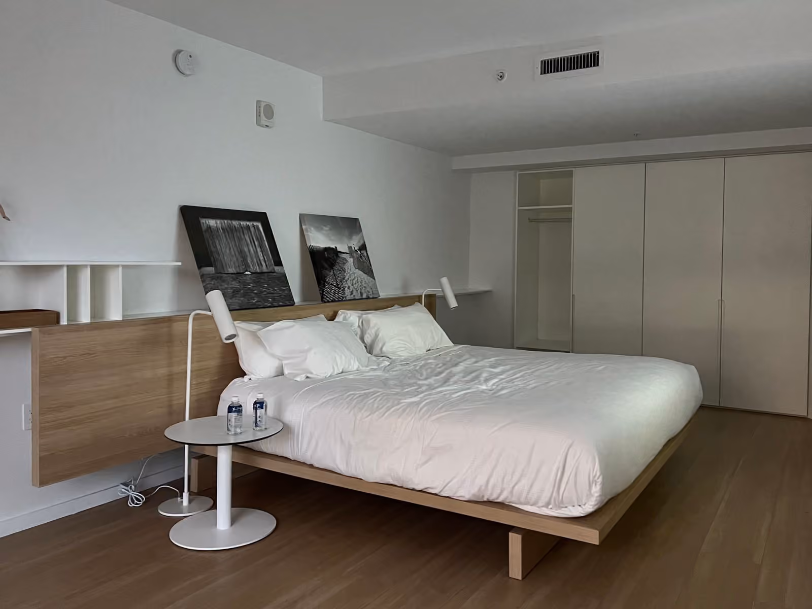 Une chambre sobre aux murs blancs, lit en bois clair, rien sur les surfaces sinon deux bouteilles d’eau.
