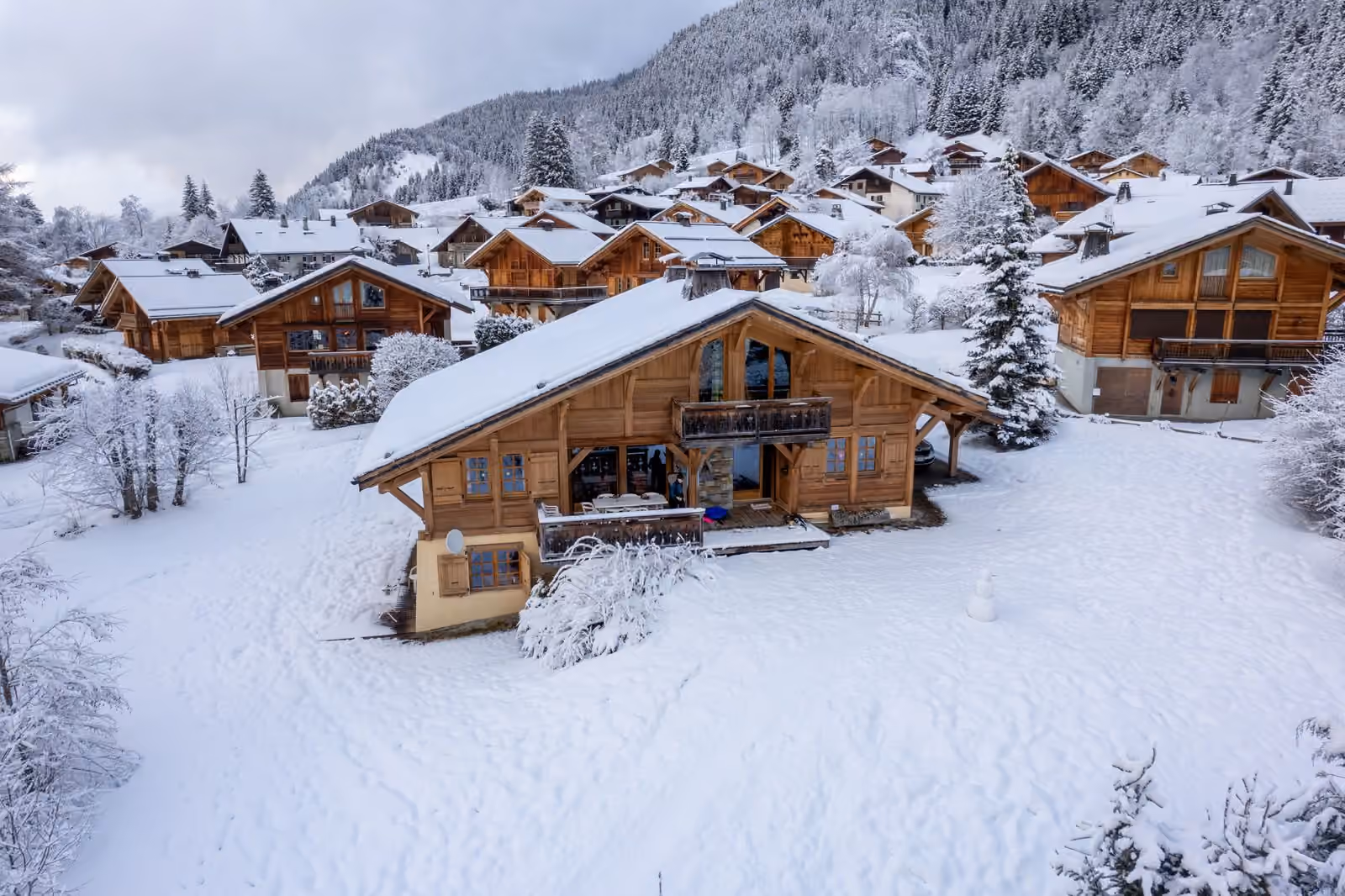 Des chalets en bois aux toits lourdement enneigés, groupés sur un versant boisé.
