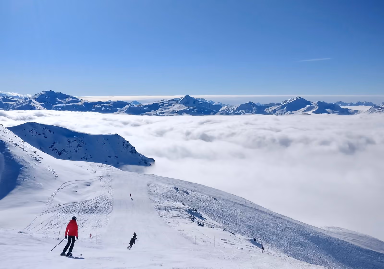Skieurs sur une piste d’altitude à Val Thorens, dominant une mer de nuages et des sommets lointains.